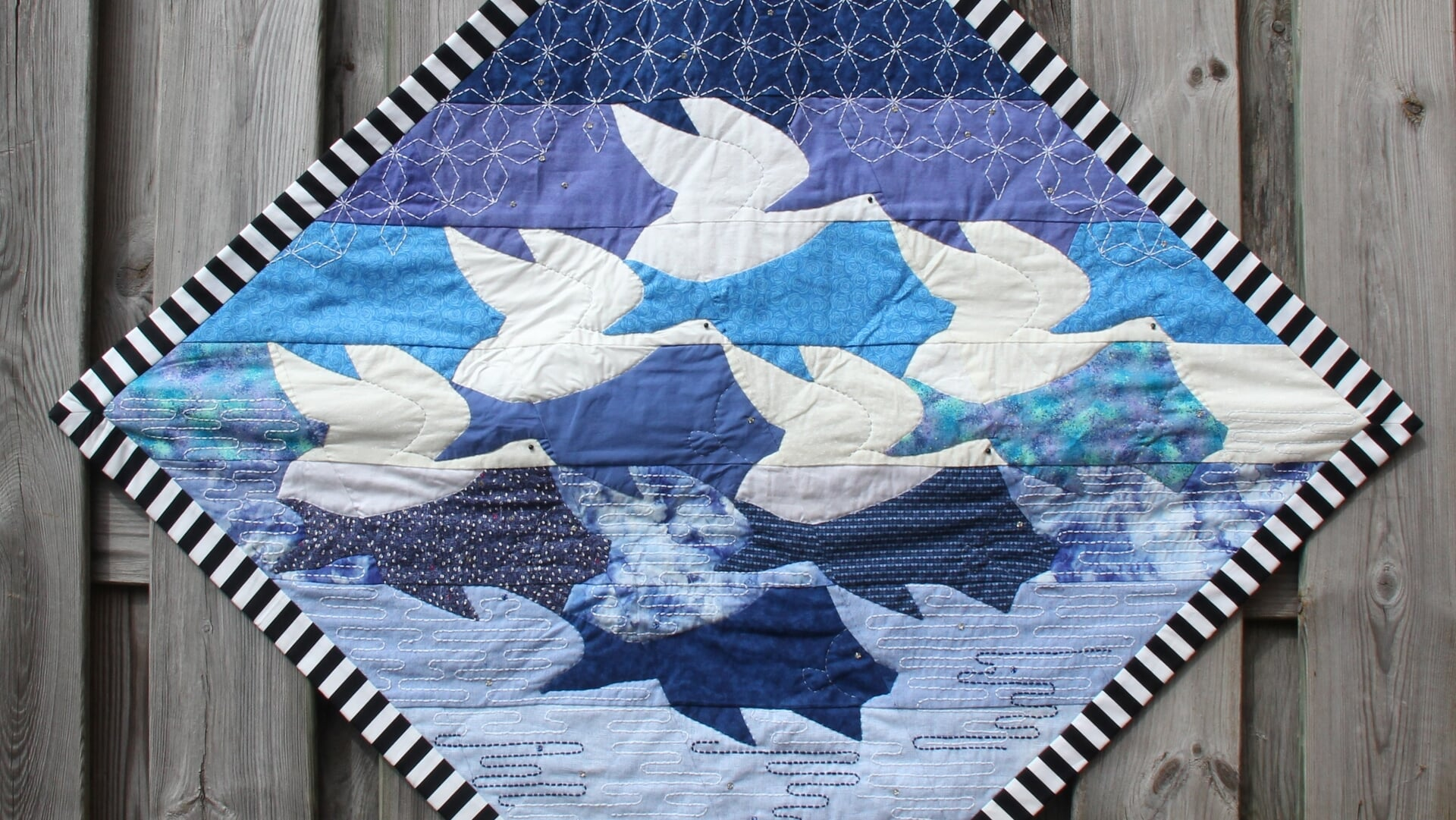 Foto van quilt met Escher uitstreling vissen en vogels in wit-blauw tinten